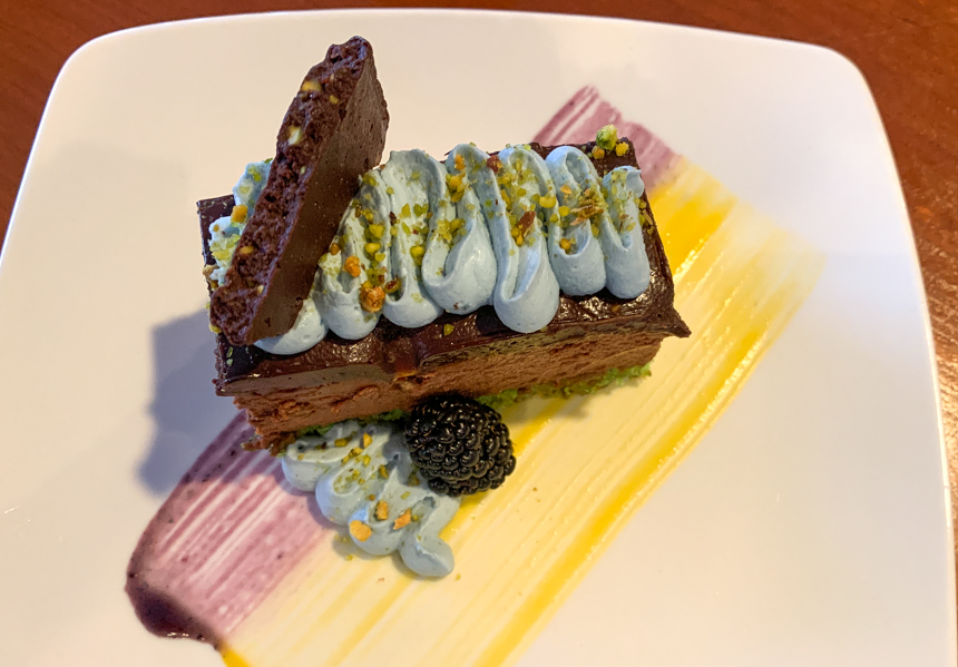 Dessert item of cholate mousse cake with rainbow colored sauces and black berries, 