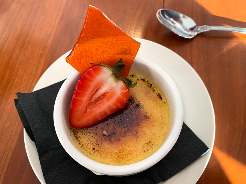 Dessert of caramelized pudding with cut red strawberry and a red sugar glass. 