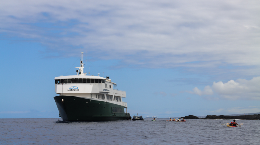 uncruise Small ship accord with kayakers venturing around the boat and rocks surrounding 