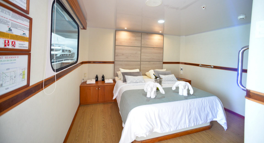 A double bed inside cabin 7 of Seaman Journey catamaran in Galapagos, wood end table, and headboard.