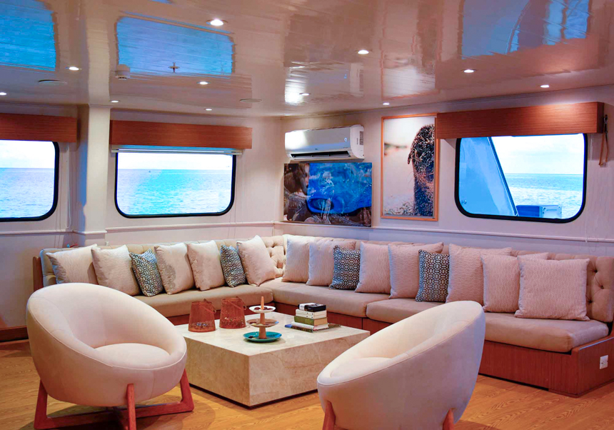 The indoor lounge and saloon aboard Seaman Journey with bench couch seating and two accent chairs around a coffee table.