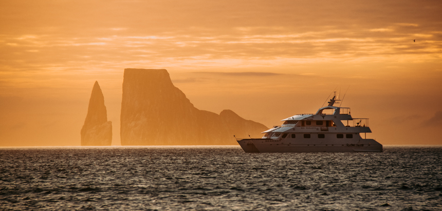 A deep orange sunset over a silhouetted kicker rock and Seaman Journey floats on the horizon line in the Galapagos.