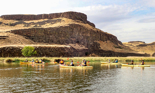 A group of kayakers on the Snake River with a red-rock cliff mountain behind them