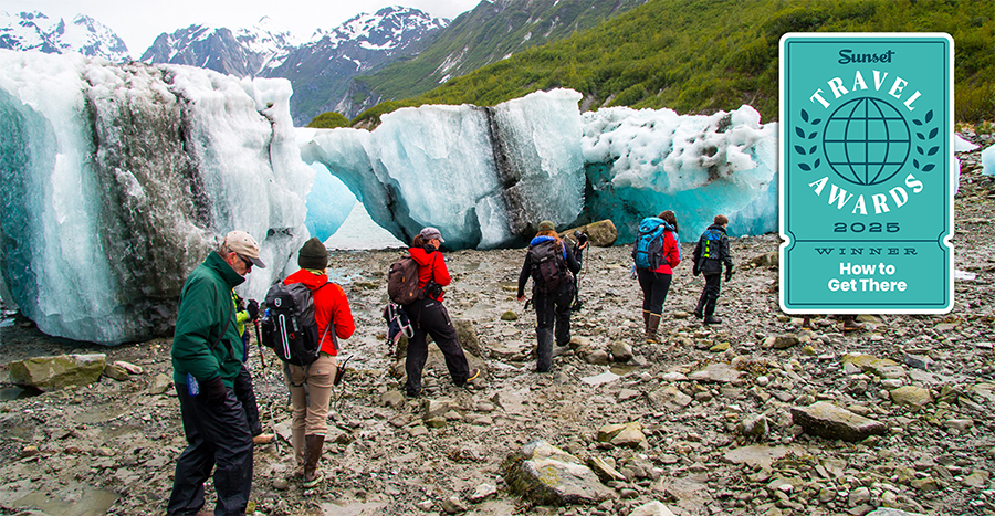 Group of travelers in Alaska walking by massive teal icebergs that have washed ashore.