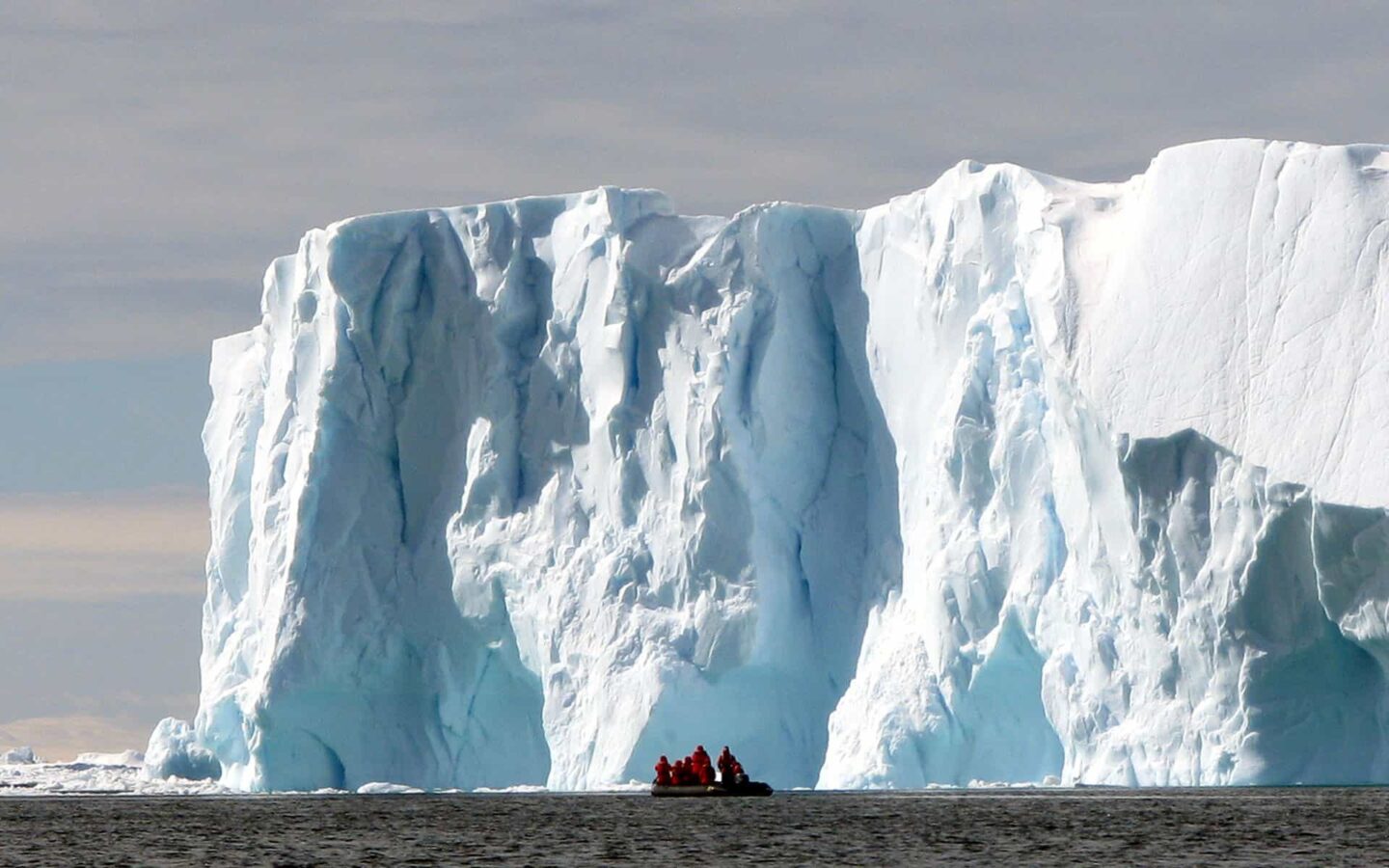 adventure travelers in a motorized raft cruising in front of a large bright iceberg on a sunny day in antarctica