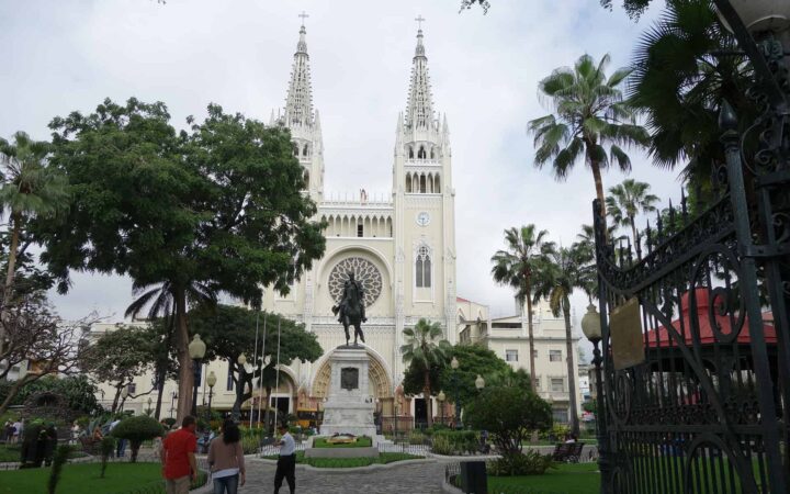 white church with two towers in guayaquil with ecuador travelers walking around it and trees in the foreground