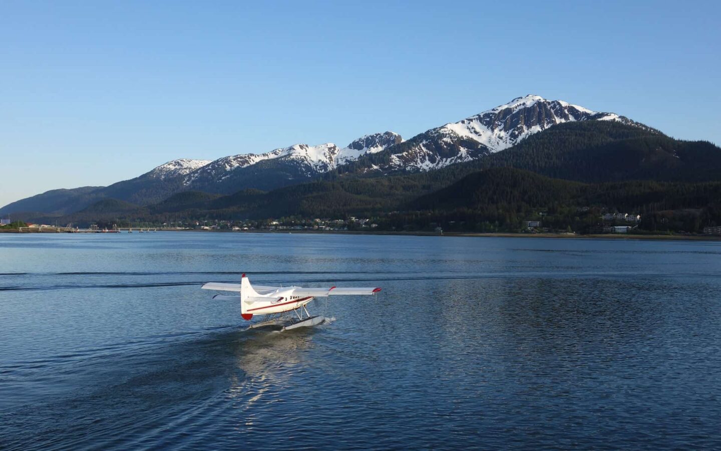 alaska sea plane lands on calm water with mountains in the distance on a sunny day