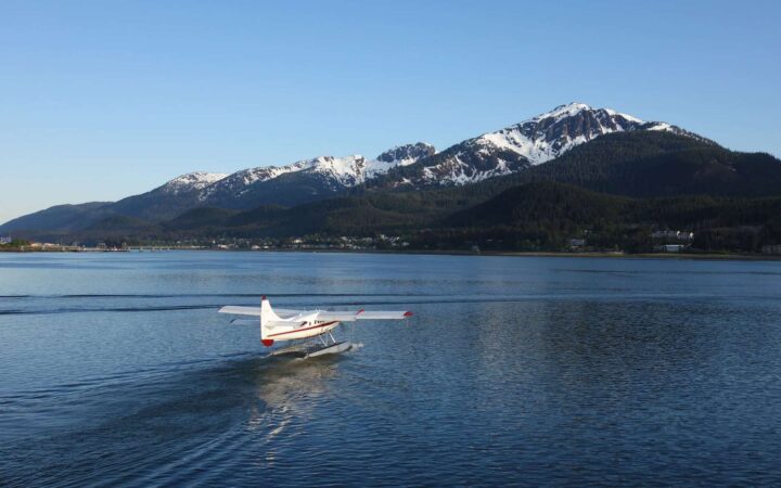alaska sea plane lands on calm water with mountains in the distance on a sunny day