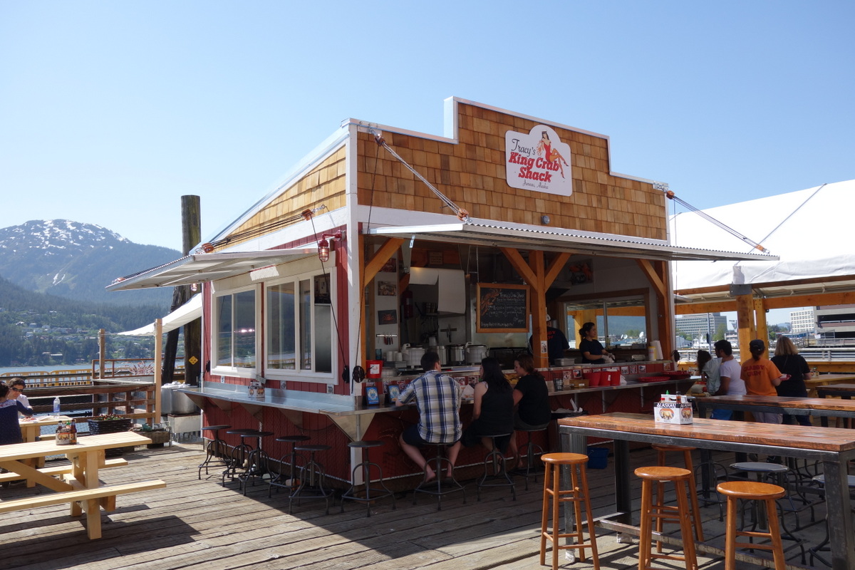 A small building at Tracy's Crab Shack in Juneau showing bar seating and picnic tables around it on a sunny day