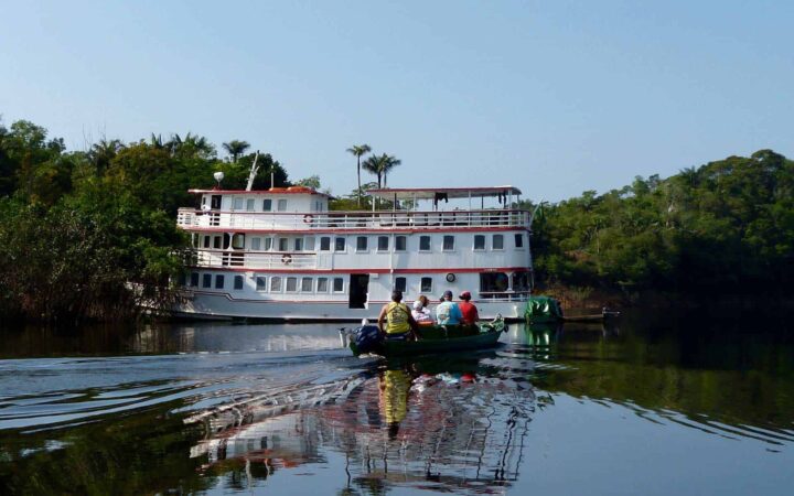 group of adventure travelers on a zodiac skiff going toward an anchored amazon small ship on a sunny day