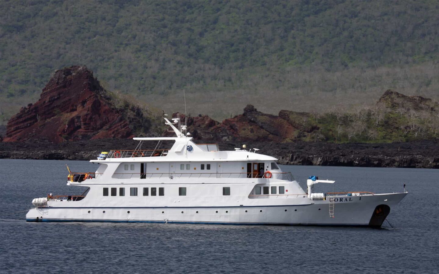 galapagos cruise charter ship anchored on calm water on a sunny day with rocks and mountains behind it
