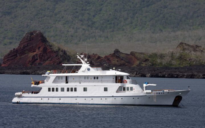 galapagos cruise charter ship anchored on calm water on a sunny day with rocks and mountains behind it