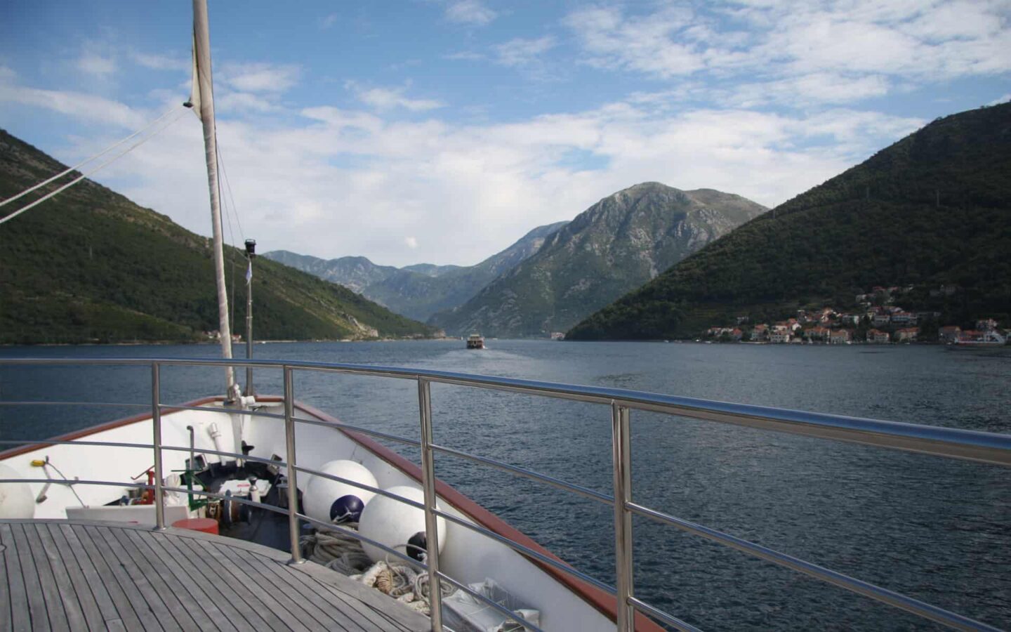 overlooking the bow of a mediterranean small ship cruising down a river with mountains on either side