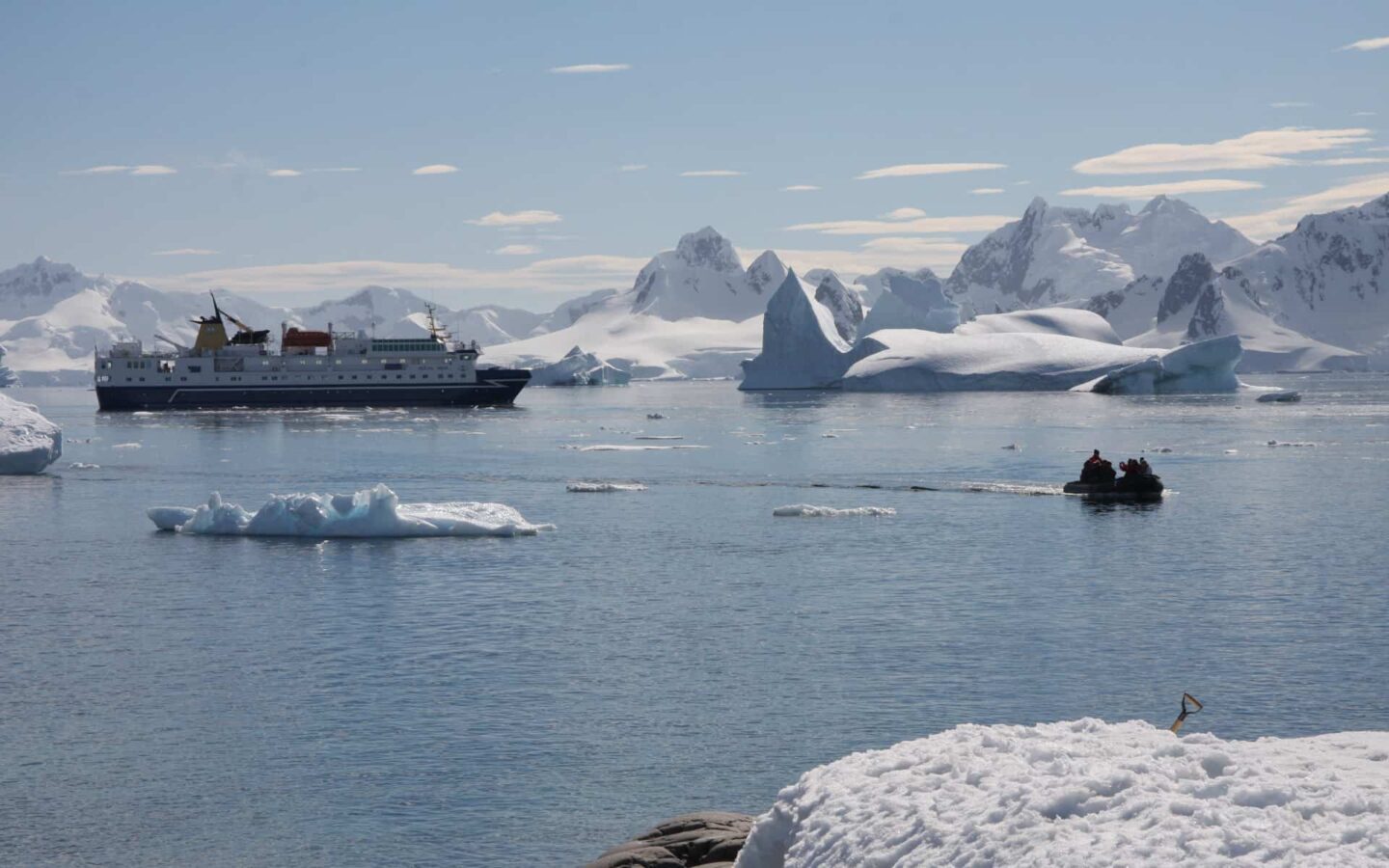 Small ship cruise in Antarctica navigating a channel with snowy landscapes and icebergs in Antarctica.