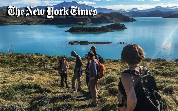 group of young people hiking patagonia on a sunny day with a lake in the foreground and huge mountains in the background