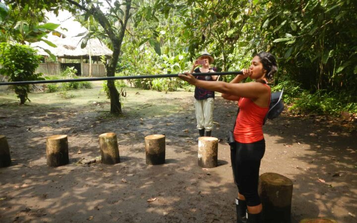 woman in a red shirt holding a blowgun to her mouth on an amazon land tour