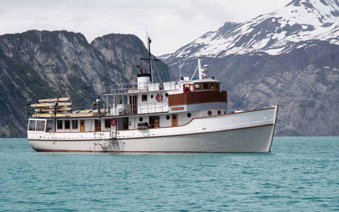 M/V sea wolf alaska small ship cruising on turquoise water with mountains behind it on a sunny day