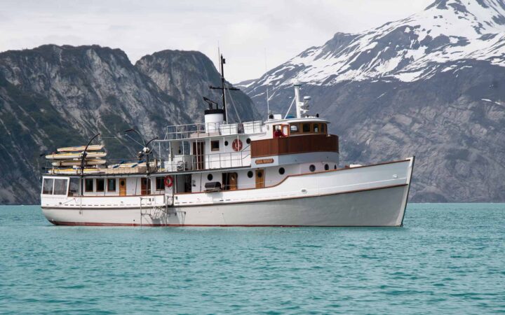 M/V sea wolf alaska small ship cruising on turquoise water with mountains behind it on a sunny day