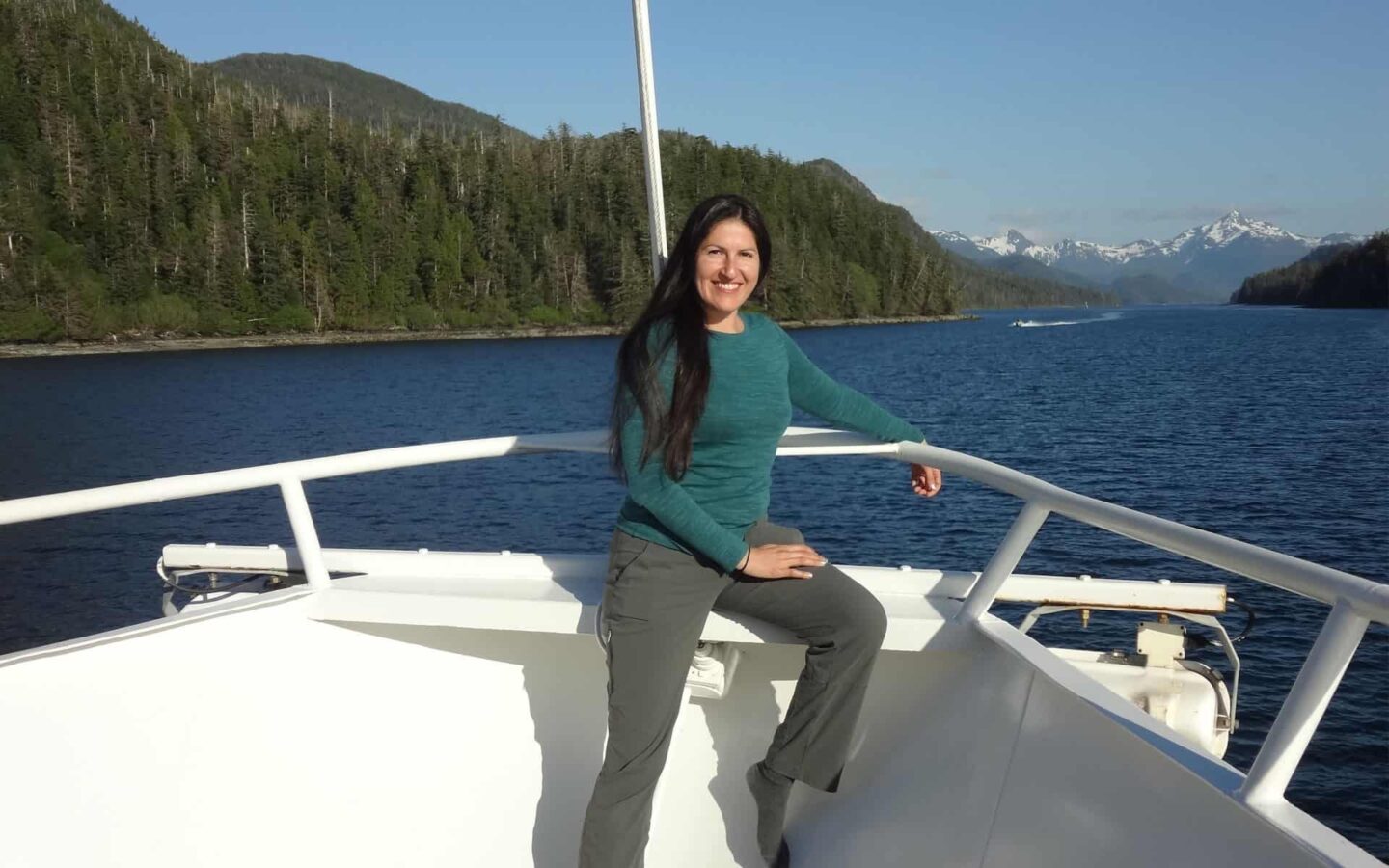 adventuresmith explorations adventure specialist leslie camacho sits on the bow of a luxury small ship in alaska on a sunny day with mountains in the distance