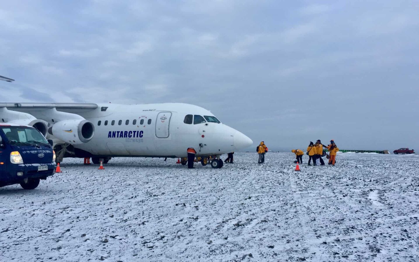 adventure travelers in yellow jackets standing next to an airplane on snow before departing on an antarctica small ship cruise