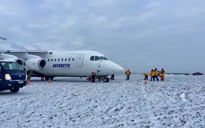 adventure travelers in yellow jackets standing next to an airplane on snow before departing on an antarctica small ship cruise