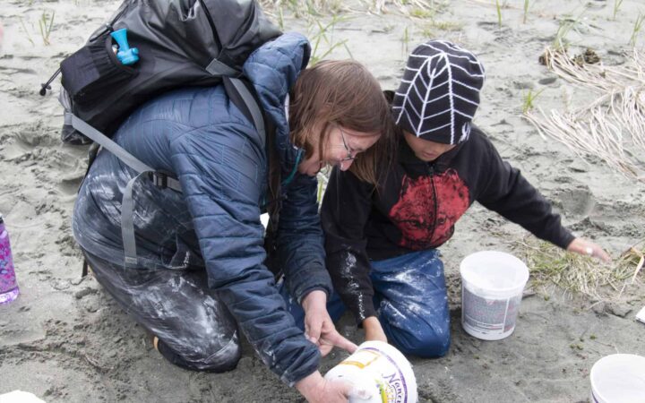 The Alaska guide leading a project with a kid on a beach with white containers.