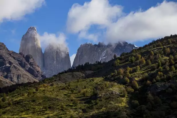 The Towers of Torres del Paine seen with wispy clouds and a green hillside in front of them