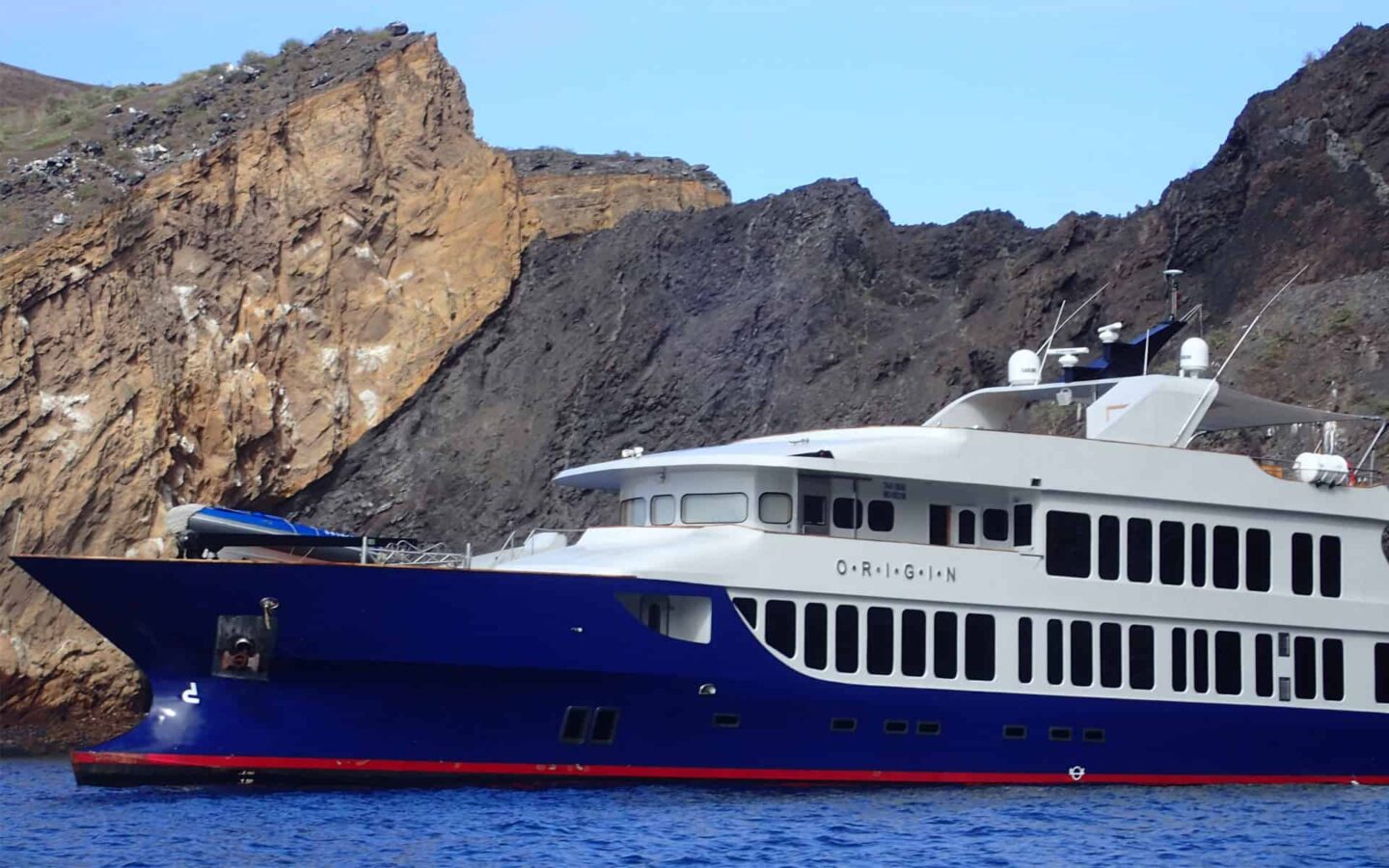 origin luxury galapagos ship sits on blue water with illuminated cliffs behind it
