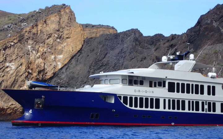 origin luxury galapagos ship sits on blue water with illuminated cliffs behind it