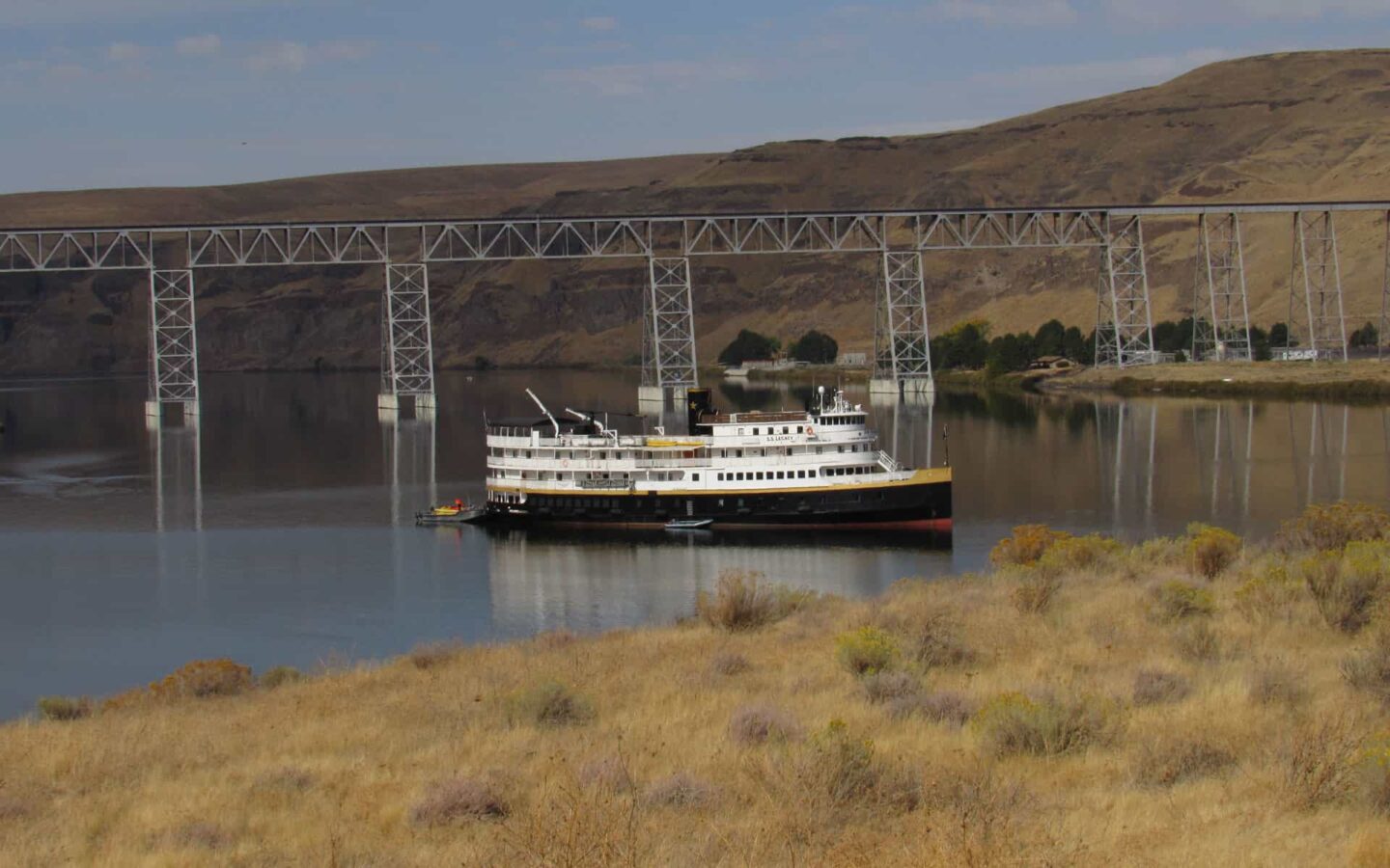 pacific northwest small ship anchored in the columbia river with a bridge behind it and brown grassy fields around it