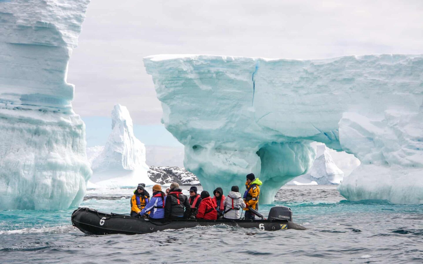 A group of travelers ride an expedition skiff among tall icebergs on a trip to Antarctica.