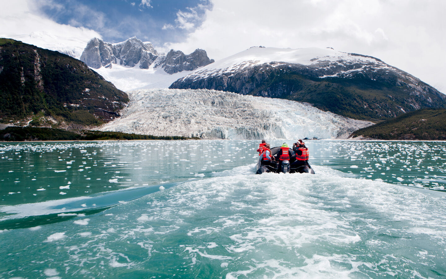 group of adventure travelers sit on the bow of a patagonia cruise ship looking at a glacier on a sunny day
