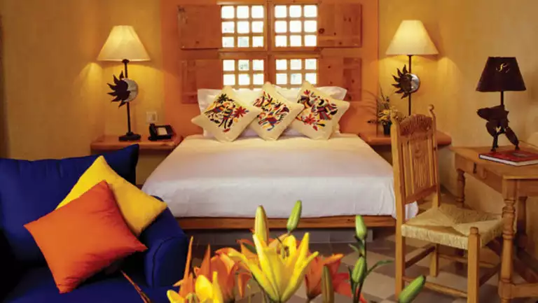 Fresh flowers near an oversized chair with small writing desk, chair, bed and windows at Casa Natalia on the Baja Peninsula