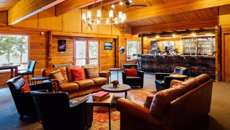 Common area with two large leather couches and four leather chairs, with bar nearby at Denali Backcountry Lodge in Kantishna, Alaska