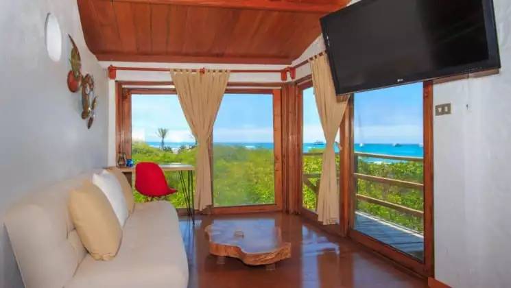 Couch, coffee table, TV, side table with stool, sliding door to balcony with ocean views at Galapagos Habitat Eco Luxury Hotel on the Galapagos Island of Santa Cruz