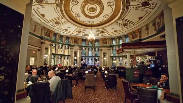 Chandelier hanging in center of dining room with diners seated in leather-backed chairs in Fort Garry Hotel in Winnipeg