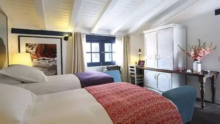Sunny room with two beds, fresh flowers on desk at El Mercado Tunqui in Cusco, Peru