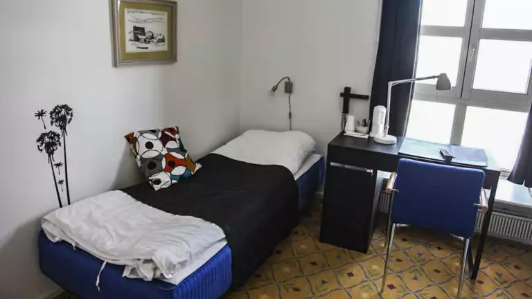 Room with bed, desk, chair, window at Hotel Angmagssalik in East Greenland
