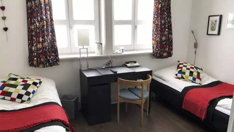 Room with two beds, desk, chair, windows at Hotel Angmagssalik in East Greenland