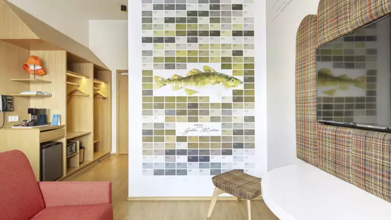 A third angle of the contemporary junior suite, with a flat-screen tv, couch, shelves, mini-fridge, at the the Icelandair Reykjavik Marina Hotel