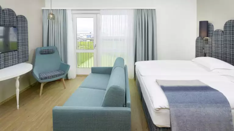 The contemporary junior suite, designed with maritime hues of blue, has a king-sized bed, couch, and television, at the the Icelandair Reykjavik Marina Hotel