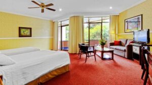 Room interior with two beds, couch, desk, coffee table, chairs, ceiling fan, TV and balcony at Hotel Bougainvillea near San Jose, Costa Rica