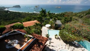 Beneath red-tiled roofs and flowering trees, the pool at Hotel La Mariposa beckons to guests with a view of the Pacific Ocean in Costa Rica