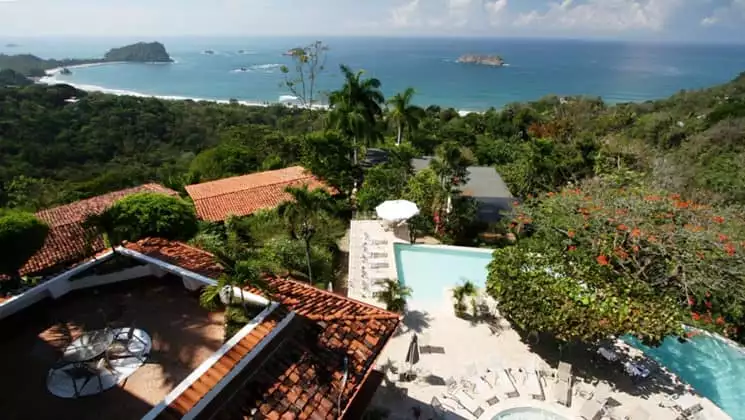 Beneath red-tiled roofs and flowering trees, the pool at Hotel La Mariposa beckons to guests with a view of the Pacific Ocean in Costa Rica