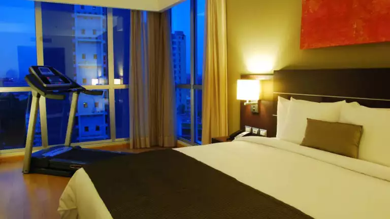 At dusk, a room with a queen-sized bed and a treadmill at the Hotel Tryp by Wyndham Panama Centro