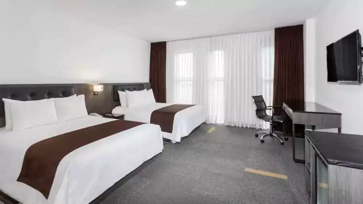 A suite with two queen-size beds, television, dresser, and large windows at the Wyndham Costa del Sol hotel, connected to the Lima International Airport