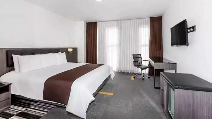 A suite with a king-sized bed, television, dresser, and large windows at the Wyndham Costa del Sol hotel, connected to the Lima International Airport