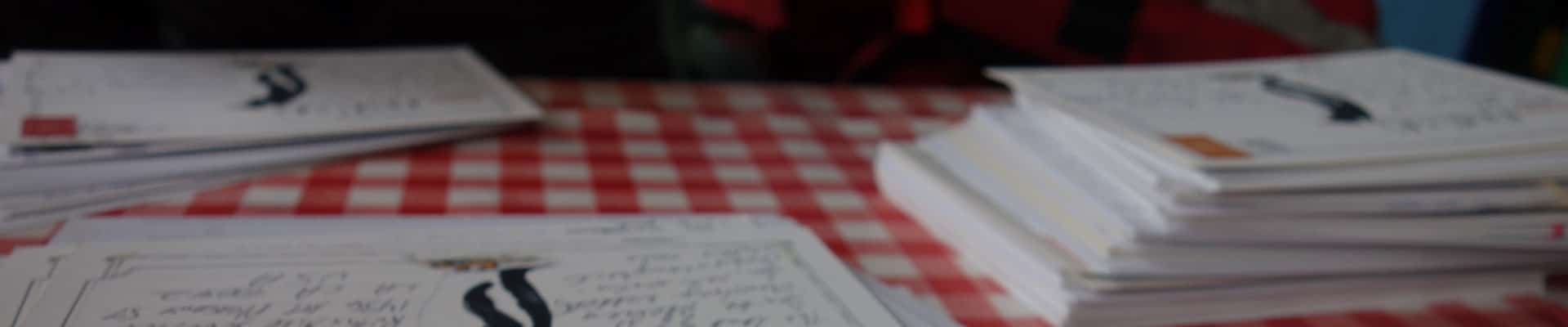 Postcards sitting in stacks on a table covered by a red-&-white checkered tablecloth.