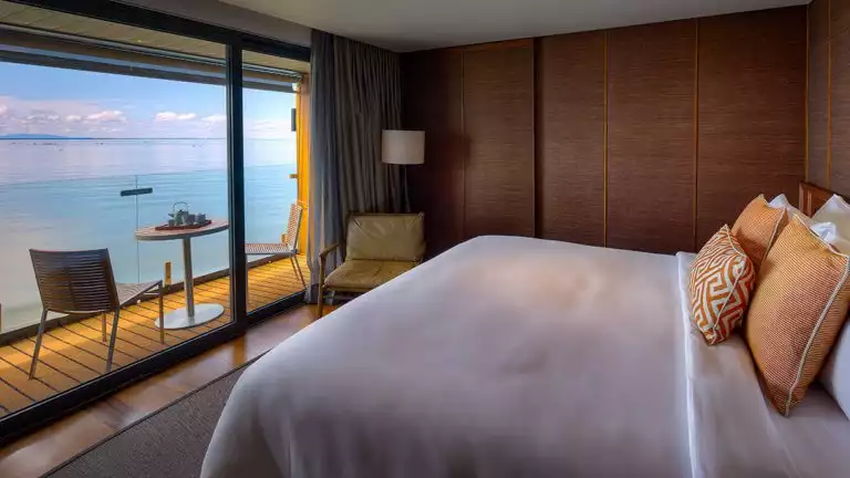 A beautiful suite on the first deck of the Aqua Mekong featuring a large bed with light linens and great views of the Mekong