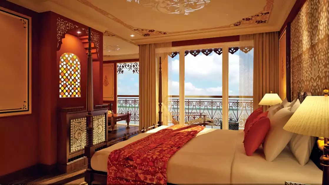 Jahan Category 3 stateroom with queen size bed, dresser, seating and outdoor balcony with chairs.